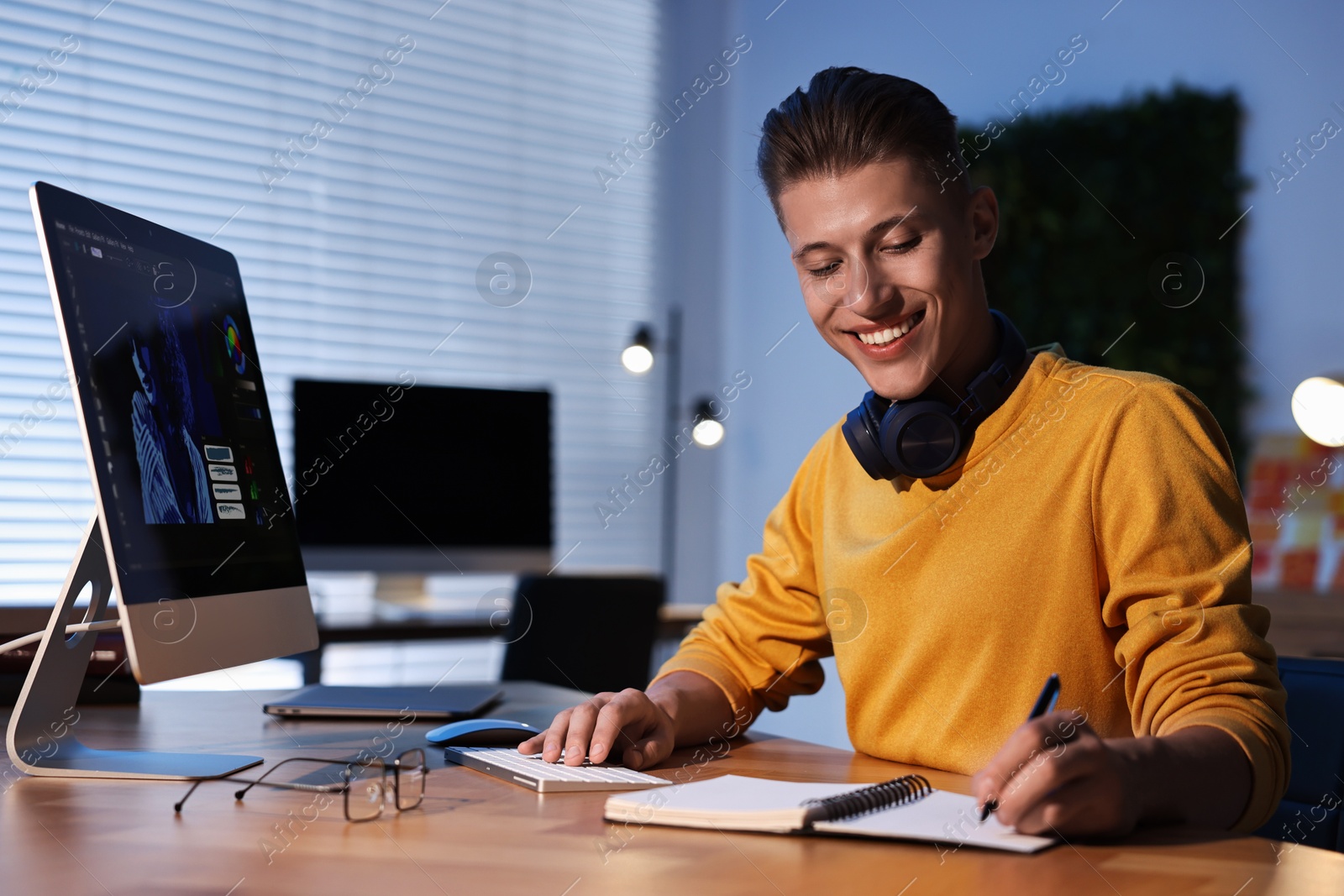 Photo of Designer taking notes while working on computer indoors at night