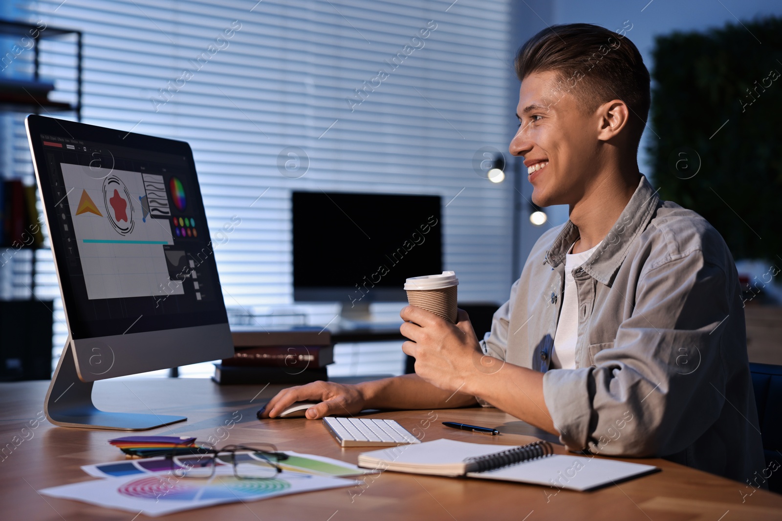 Photo of Designer with paper cup of coffee working on computer indoors at night