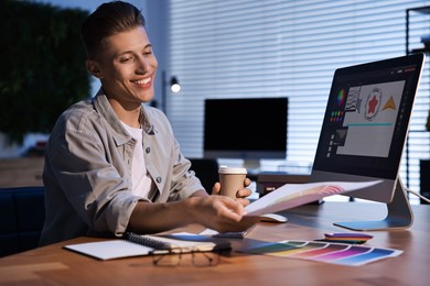 Photo of Designer with color palette and paper cup of coffee working indoors at night