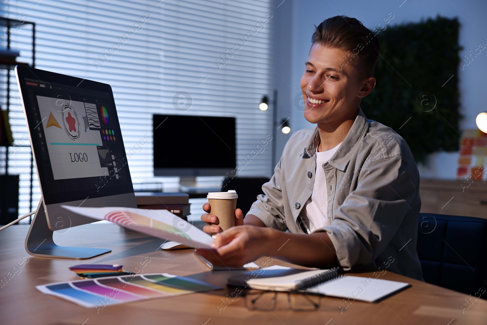 Photo of Designer with color palette and paper cup of coffee working indoors at night