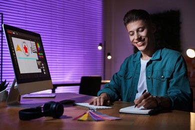 Photo of Designer taking notes while working on computer indoors at night