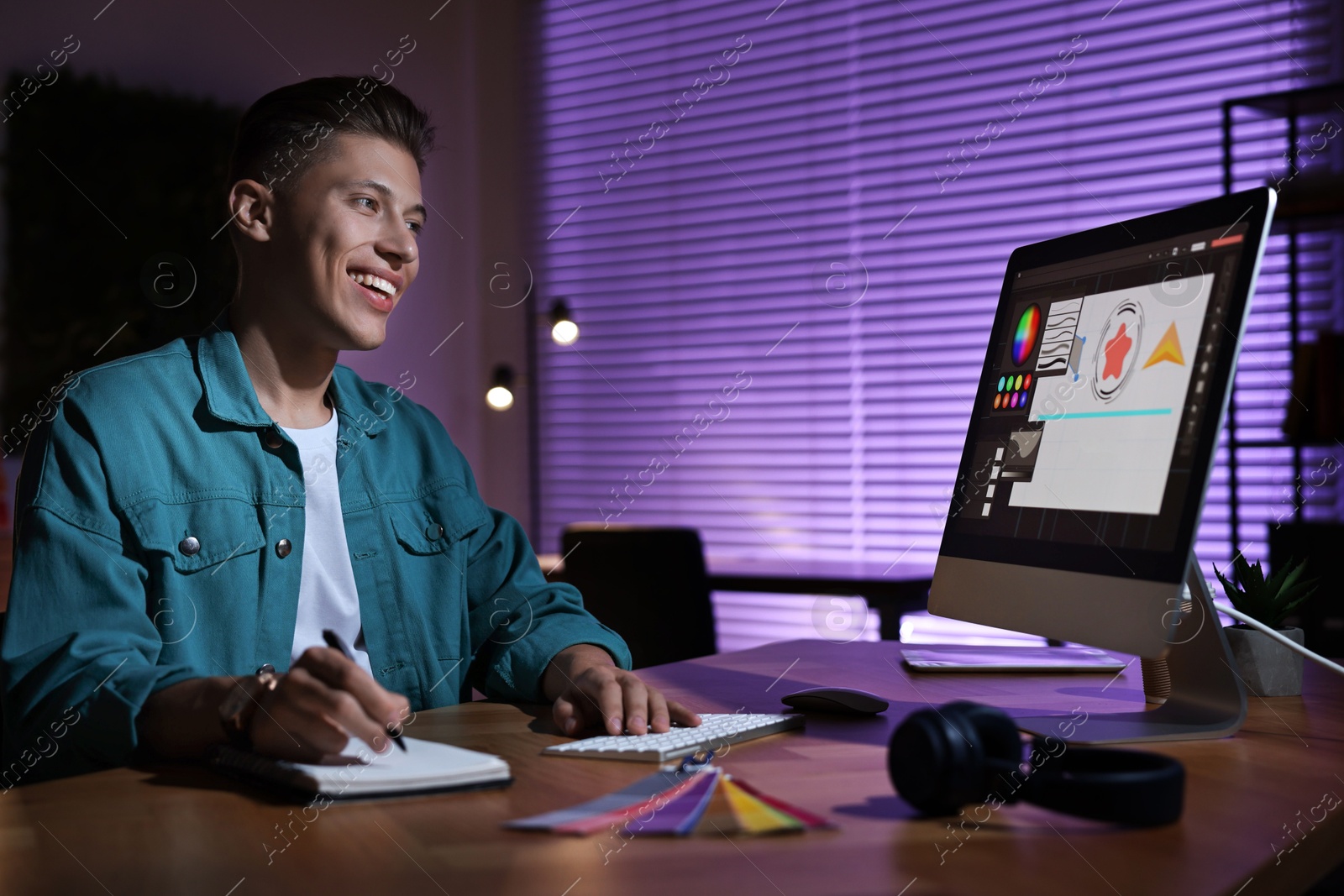 Photo of Designer taking notes while working on computer indoors at night