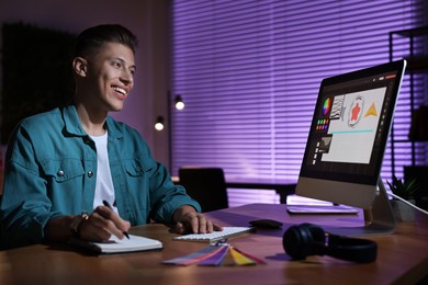 Designer taking notes while working on computer indoors at night