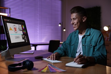 Designer taking notes while working on computer indoors at night