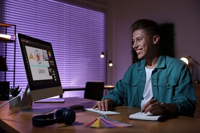 Designer taking notes while working on computer indoors at night