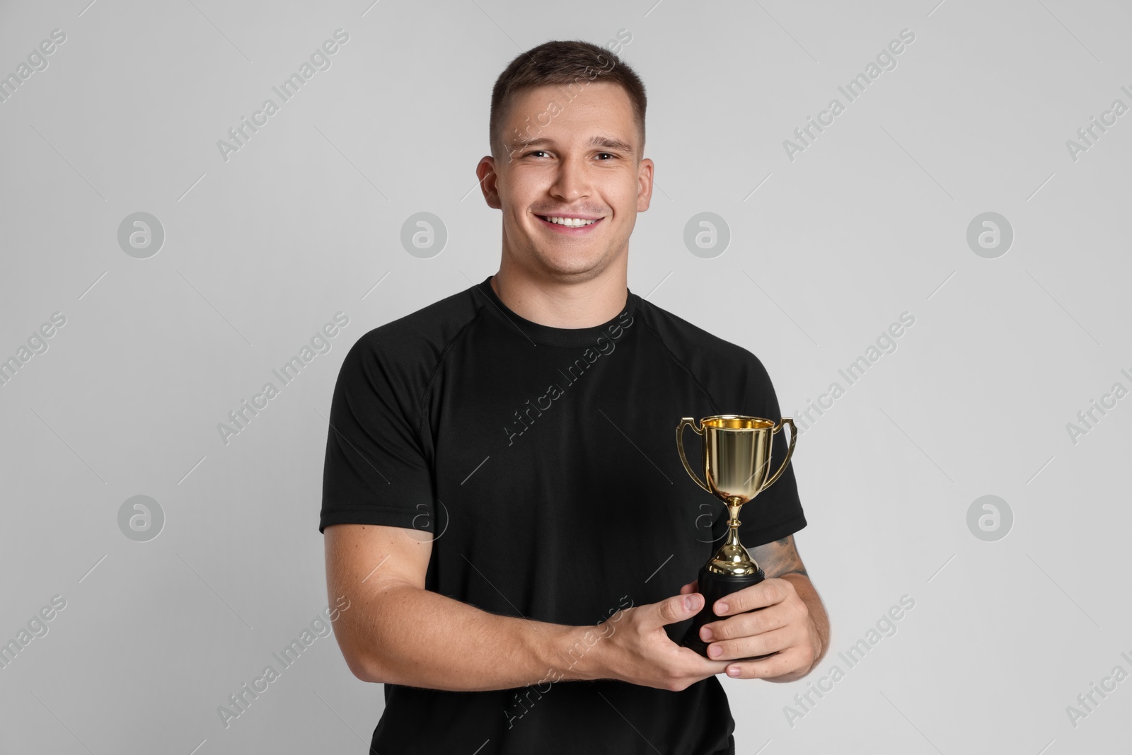 Photo of Happy winner with golden trophy cup on light grey background