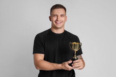 Photo of Happy winner with golden trophy cup on light grey background