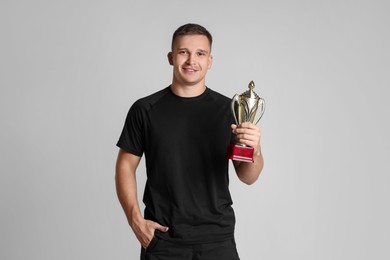 Photo of Happy winner with golden trophy cup on light grey background