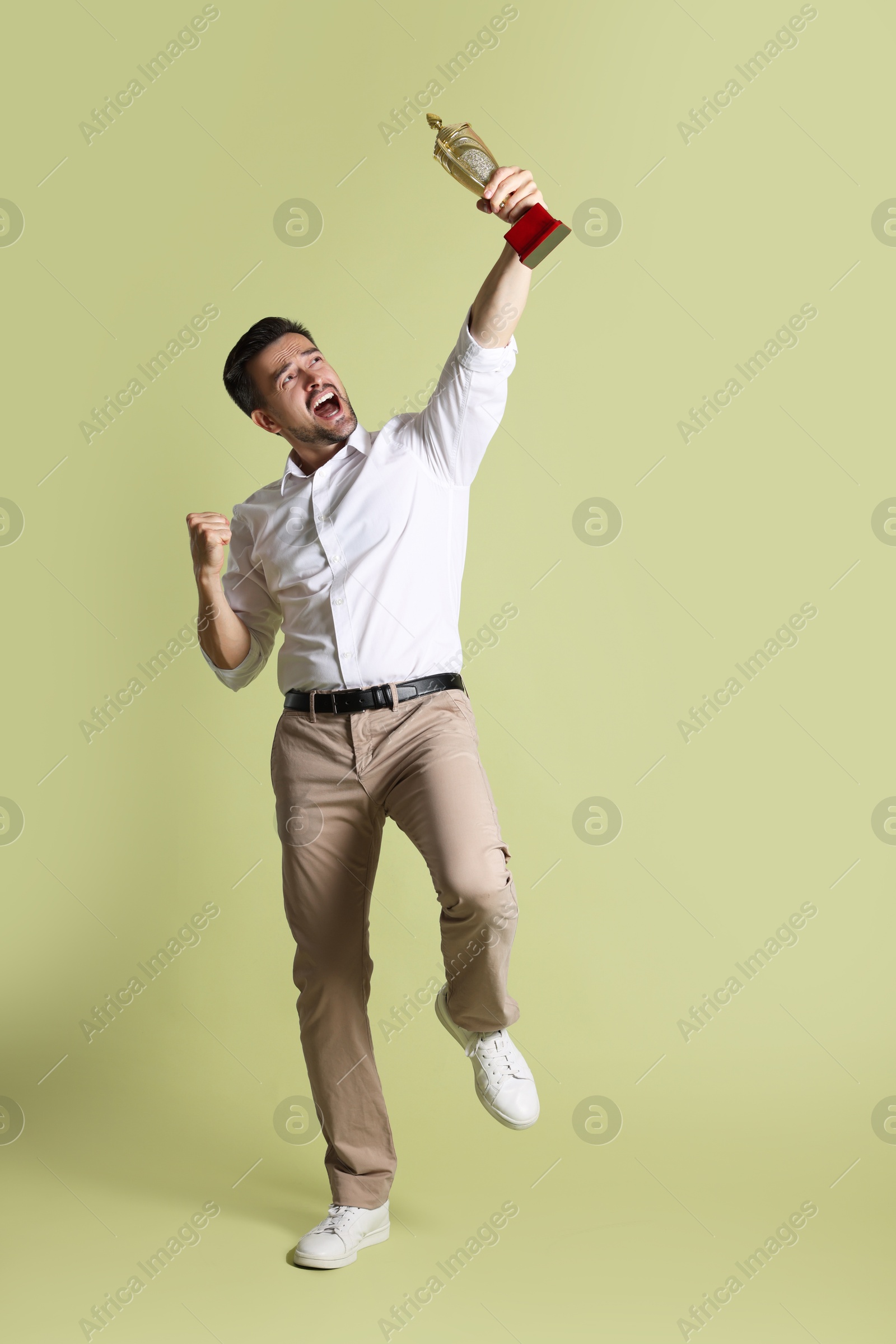 Photo of Happy winner with golden trophy cup on pale olive background