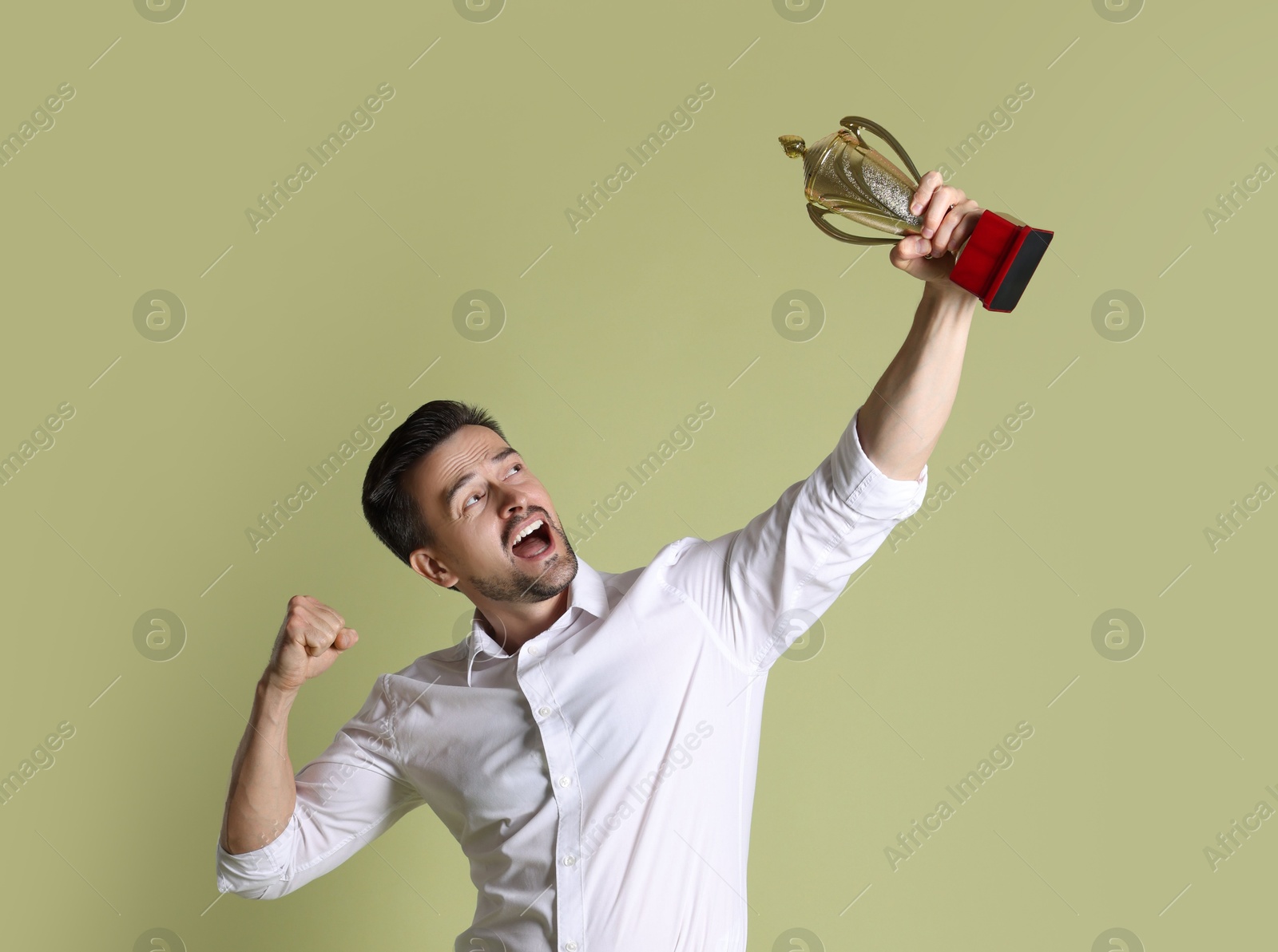 Photo of Happy winner with golden trophy cup on pale olive background