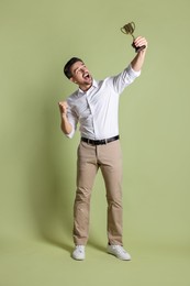 Photo of Happy winner with golden trophy cup on pale olive background