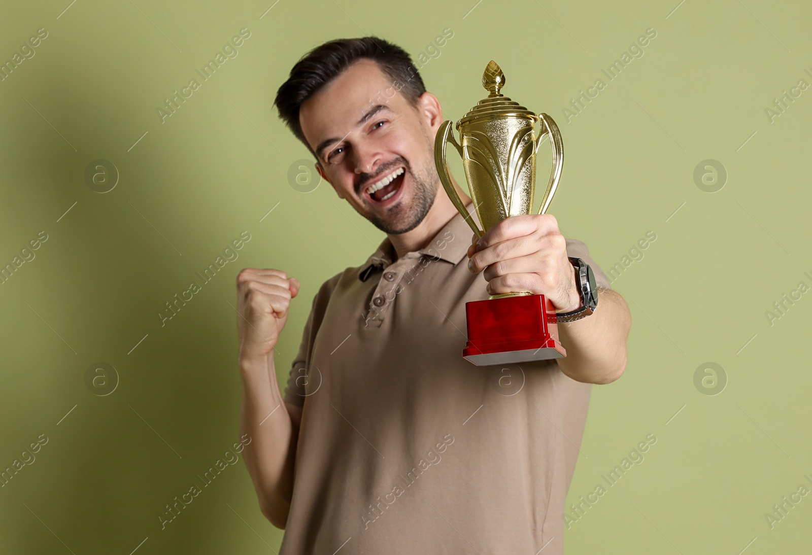 Photo of Happy winner with golden trophy cup on pale olive background