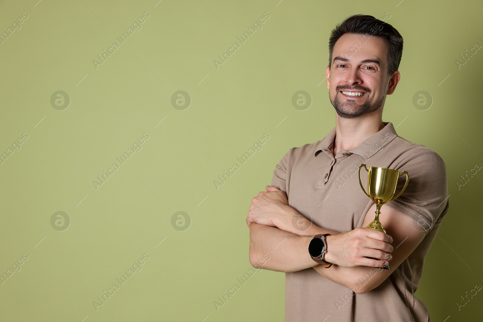 Photo of Happy winner with golden trophy cup on pale olive background, space for text