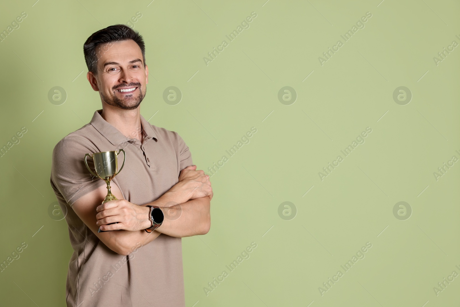 Photo of Happy winner with golden trophy cup on pale olive background, space for text