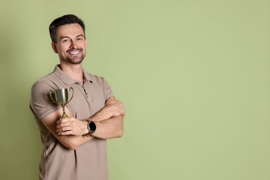 Photo of Happy winner with golden trophy cup on pale olive background, space for text