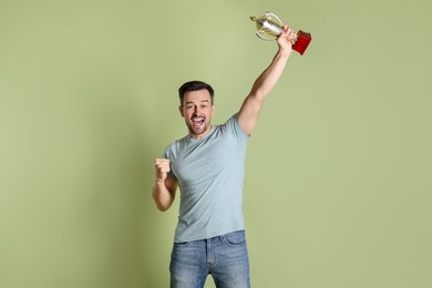 Photo of Happy winner with golden trophy cup on pale olive background