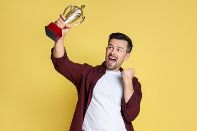 Photo of Happy winner with golden trophy cup on yellow background