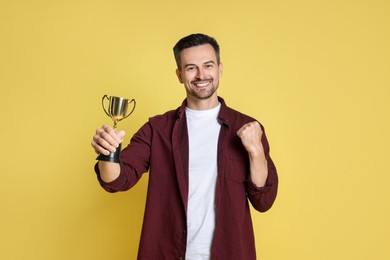 Photo of Happy winner with golden trophy cup on yellow background