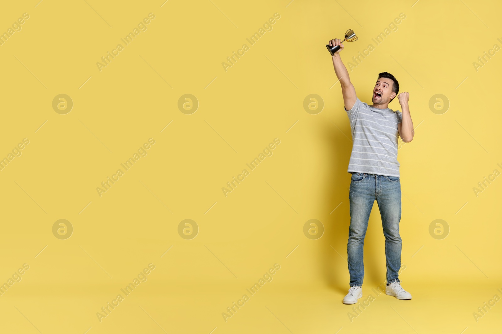 Photo of Happy winner with golden trophy cup on yellow background