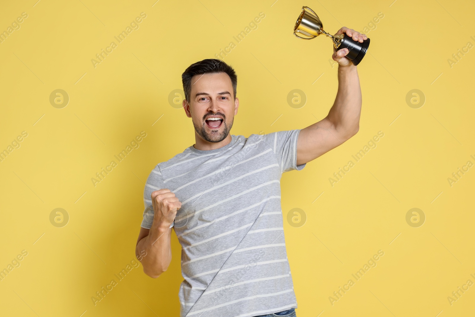 Photo of Happy winner with golden trophy cup on yellow background