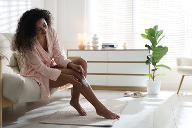 Photo of Young woman applying cream onto leg on sofa at home