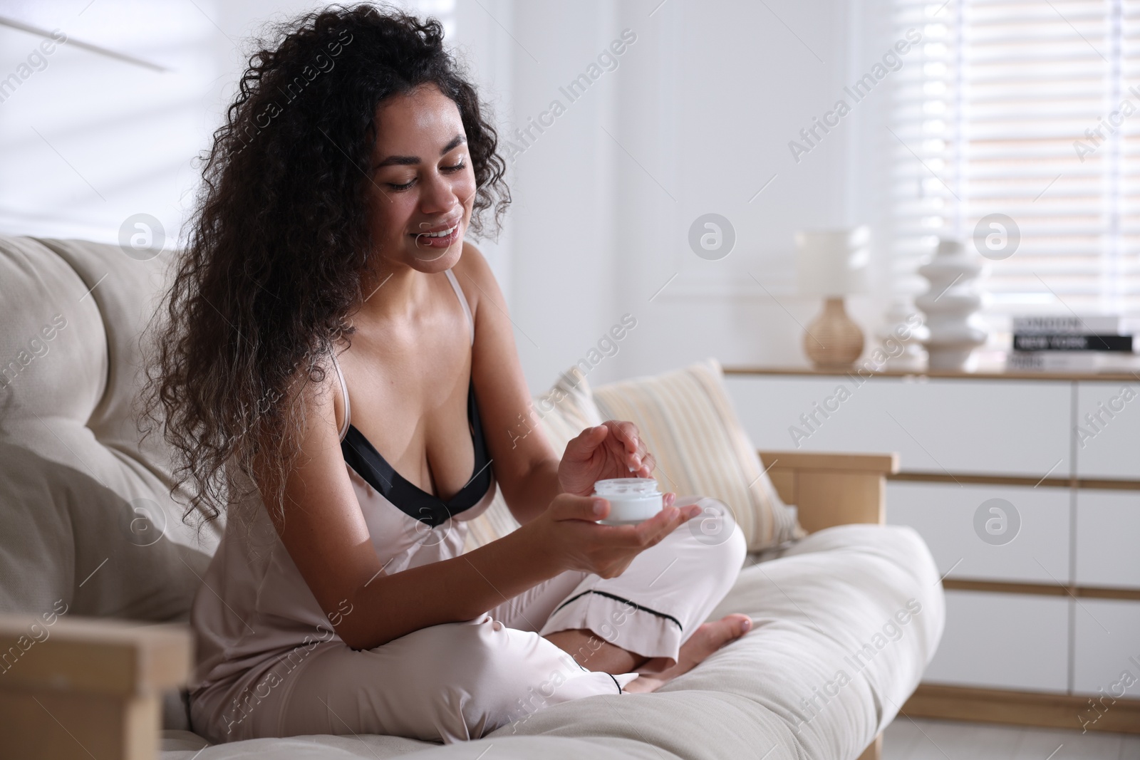 Photo of Young woman with jar of cream on sofa at home. Space for text