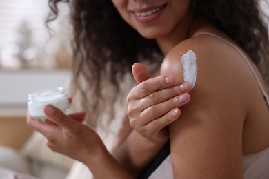 Woman applying cream onto shoulder at home, closeup