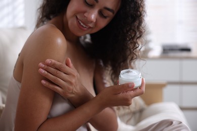 Woman applying cream onto shoulder at home, selective focus