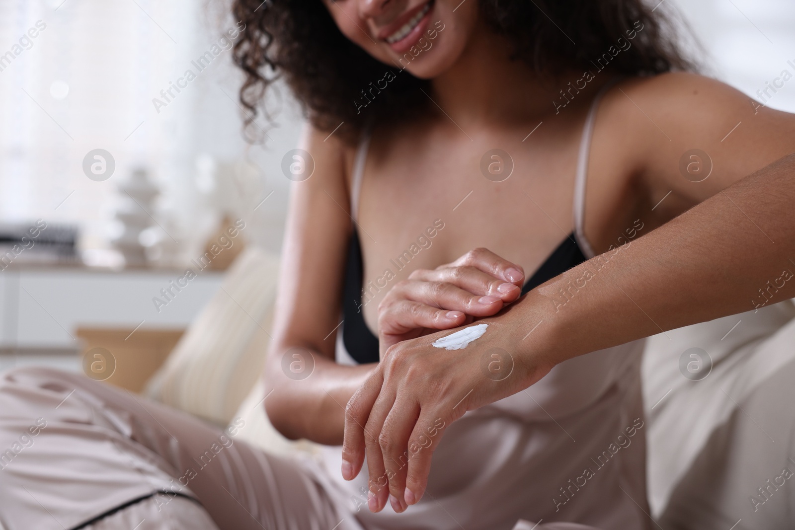 Photo of Young woman applying cream onto hand on sofa at home, closeup