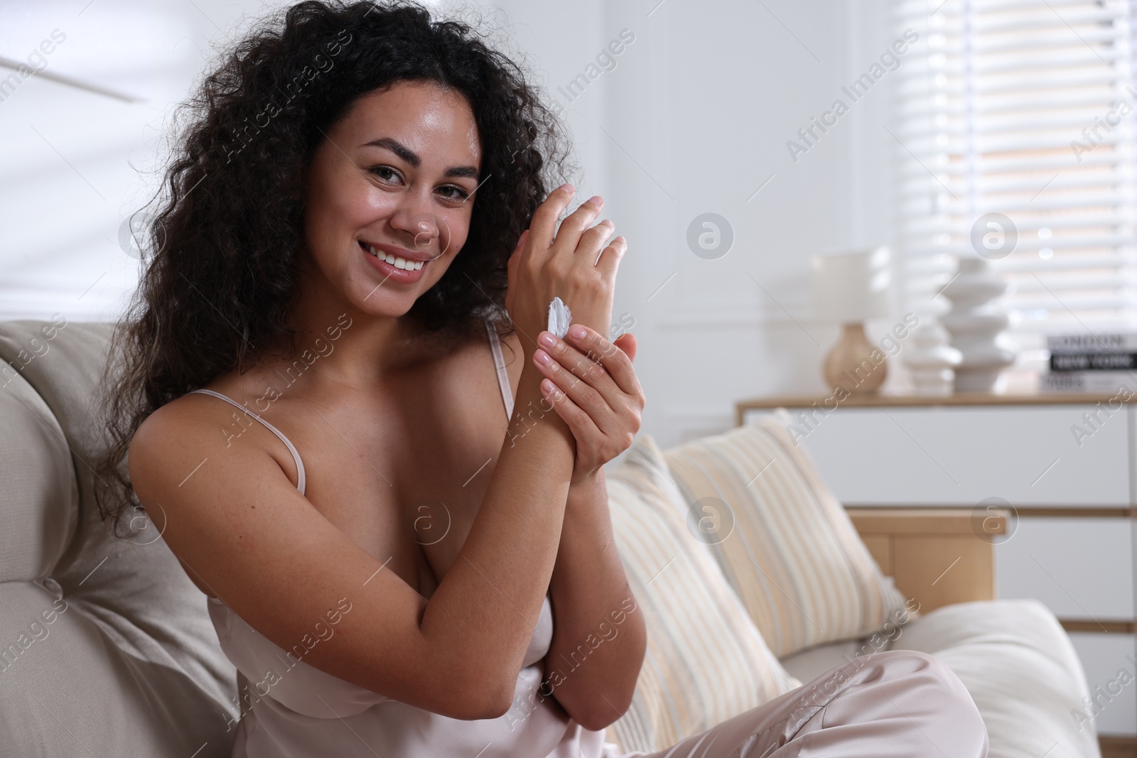 Photo of Beautiful woman applying cream onto hand on sofa at home. Space for text