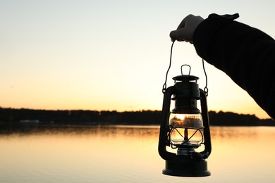 Photo of Man with vintage kerosene lamp near river in evening, closeup. Space for text