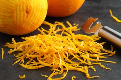 Photo of Fresh orange zest, zester and fruits on black table, closeup