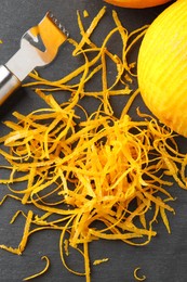 Photo of Fresh orange zest, zester and fruit on black table, flat lay