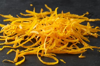 Photo of Pile of fresh orange zest on black table, closeup