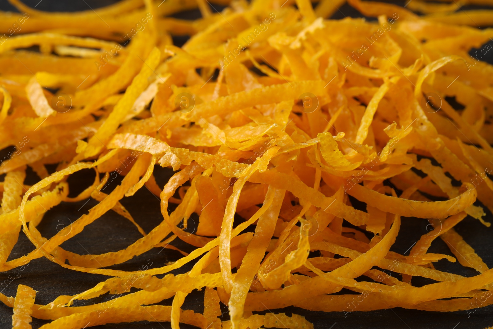 Photo of Pile of fresh orange zest on black table, closeup