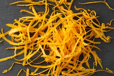 Photo of Pile of fresh orange zest on black table, top view