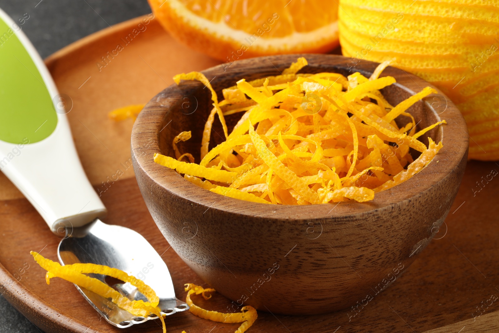 Photo of Fresh orange zest in wooden bowl and zester, closeup