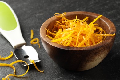 Photo of Fresh orange zest and zester on black table, closeup