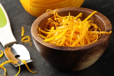 Photo of Fresh orange zest and zester on black table, closeup