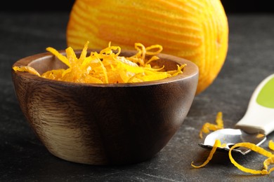 Photo of Fresh orange zest, zester and fruit on black table, closeup