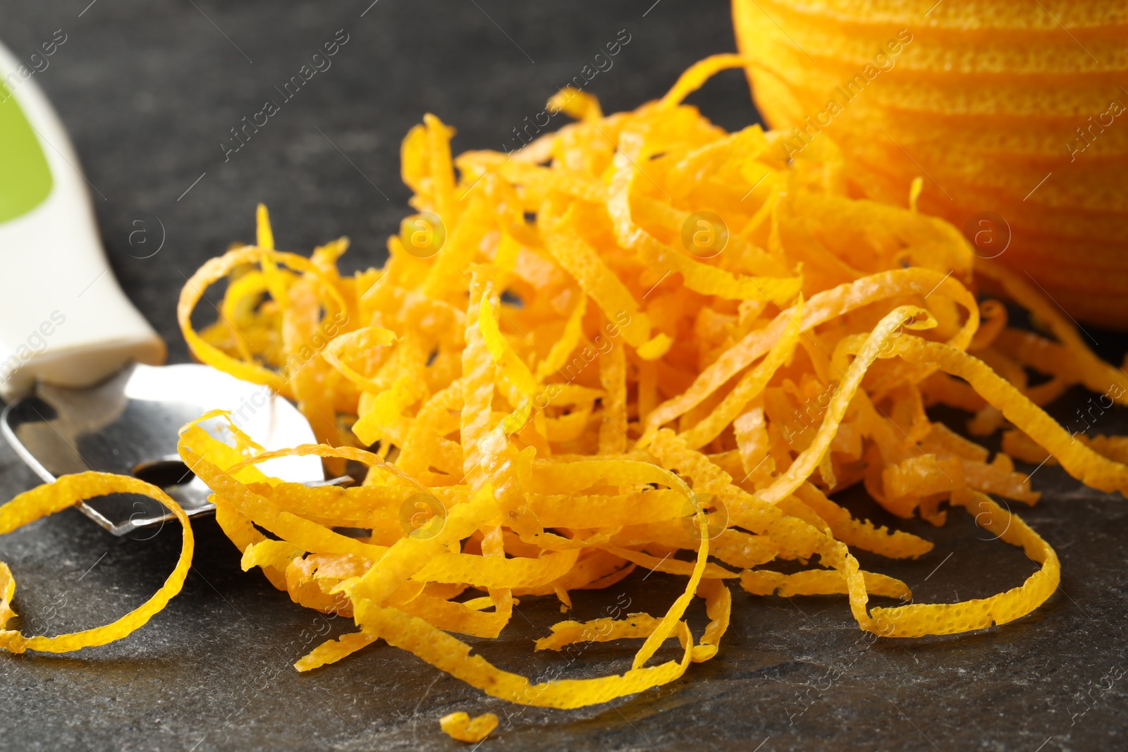 Photo of Fresh orange zest and fruit on black table, closeup