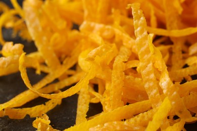 Photo of Pile of fresh orange zest on black table, closeup