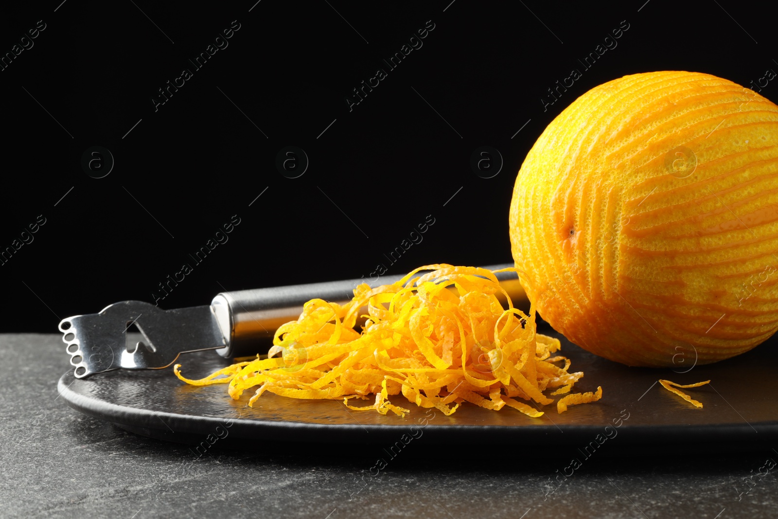 Photo of Fresh orange zest, zester and fruit on black table, closeup. Space for text