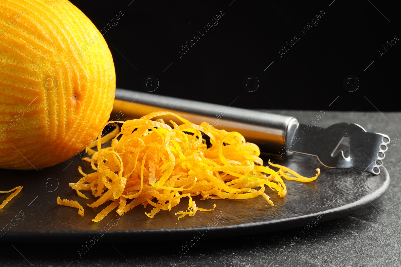 Photo of Fresh orange zest, zester and fruit on black table, closeup