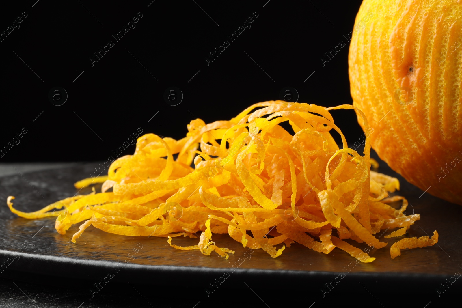 Photo of Fresh orange zest and fruit on black table, closeup