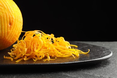 Photo of Fresh orange zest and fruit on black table, closeup