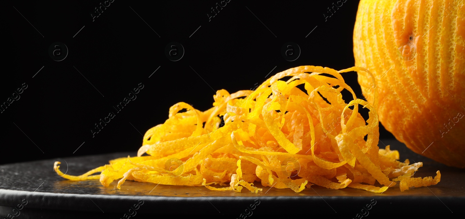 Photo of Fresh orange zest and fruit on black table, closeup. Space for text