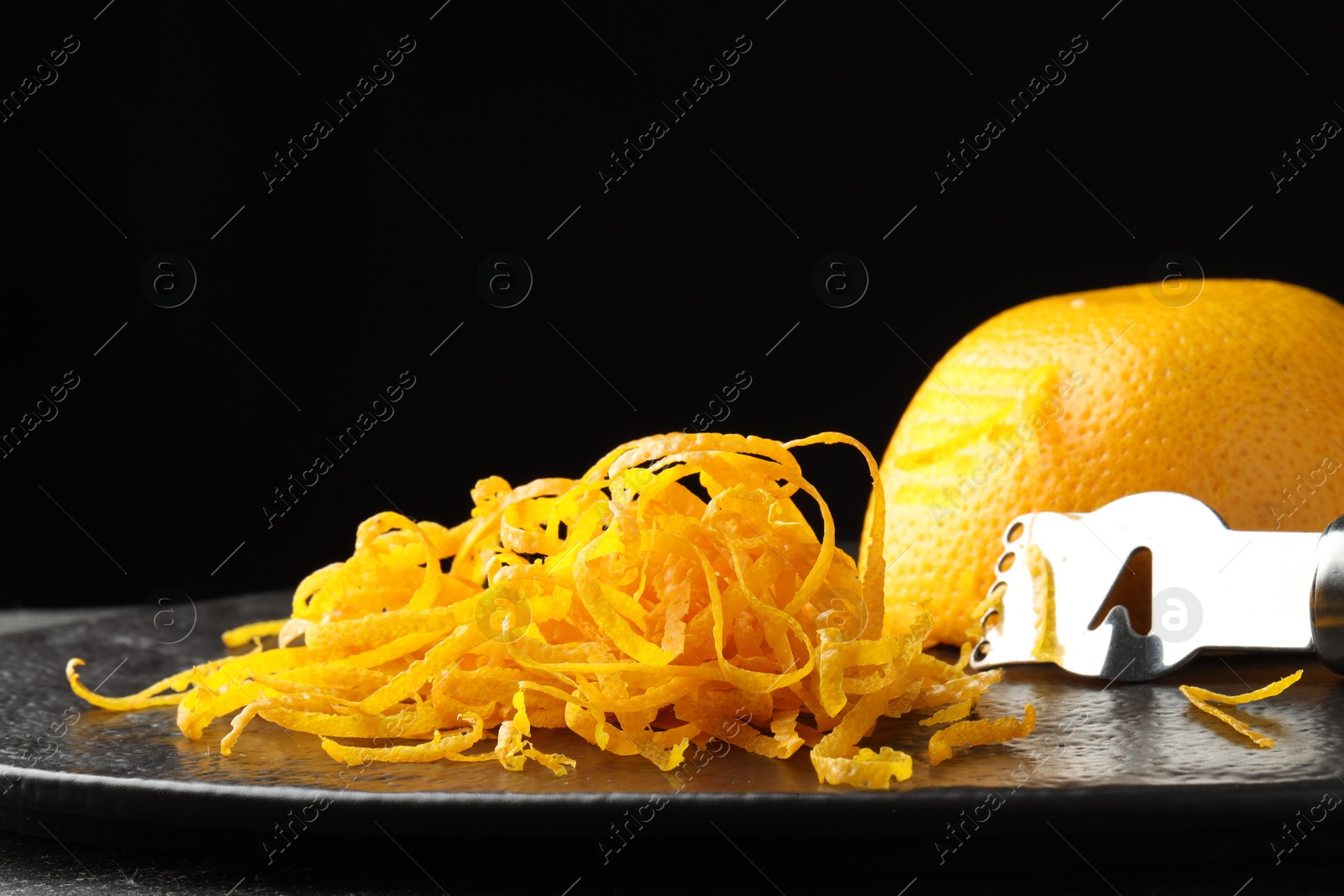 Photo of Fresh orange zest, zester and fruit on black table, closeup. Space for text