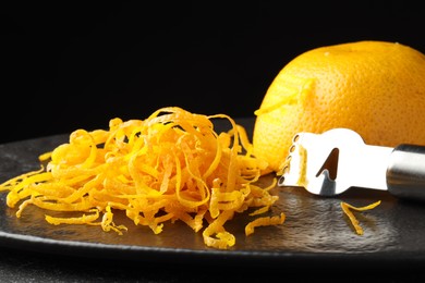 Photo of Fresh orange zest, zester and fruit on black table, closeup