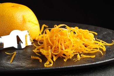 Photo of Fresh orange zest, zester and fruit on black table, closeup